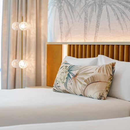 布里斯班阿莫拉酒店 外观 照片 The photo shows a stylish hotel room featuring two neatly made beds with white linens. Each bed has several pillows, one of which has a decorative cover with a tropical plant pattern. Behind the beds is a modern headboard, and the wall is decorated w