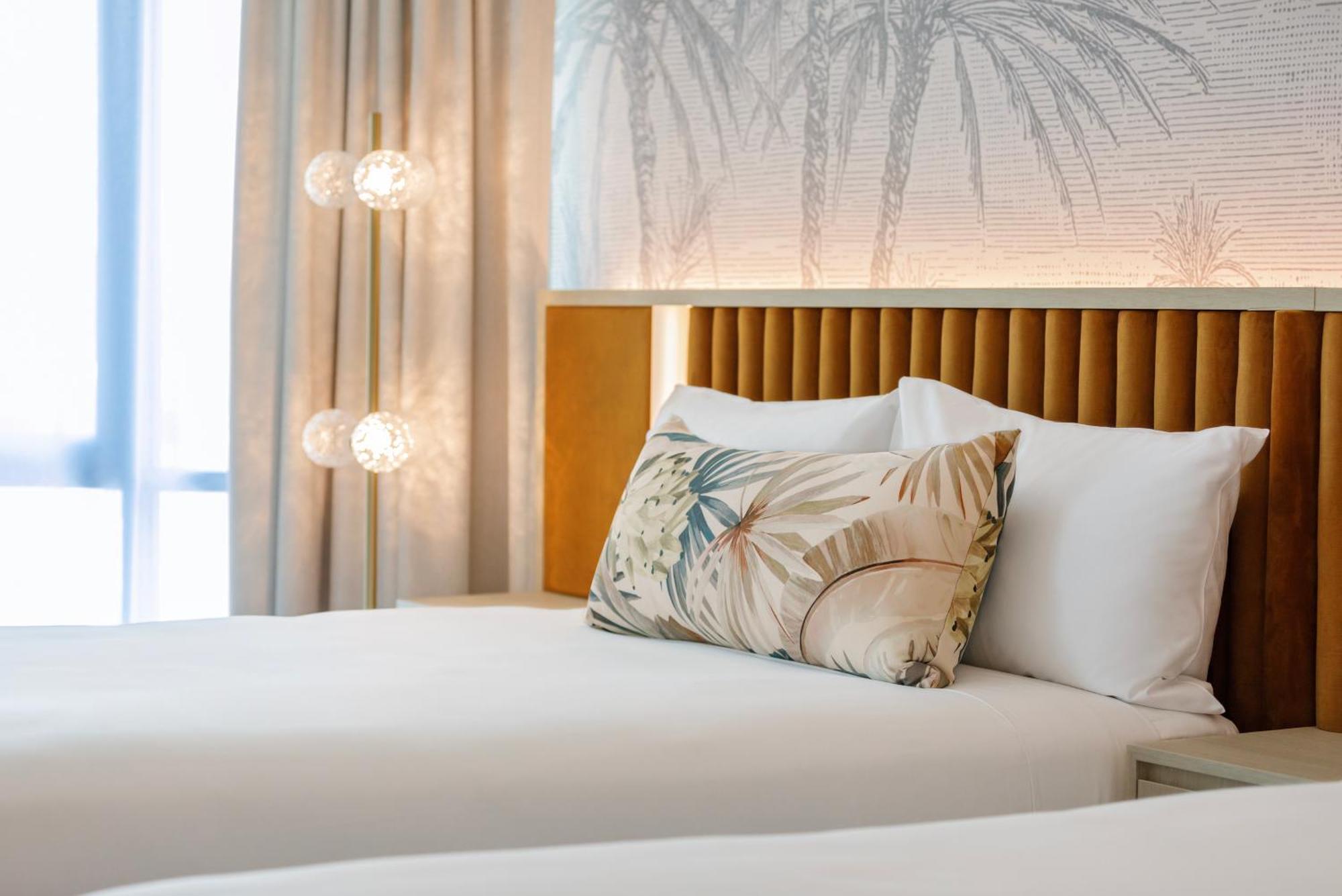 布里斯班阿莫拉酒店 外观 照片 The photo shows a stylish hotel room featuring two neatly made beds with white linens. Each bed has several pillows, one of which has a decorative cover with a tropical plant pattern. Behind the beds is a modern headboard, and the wall is decorated w